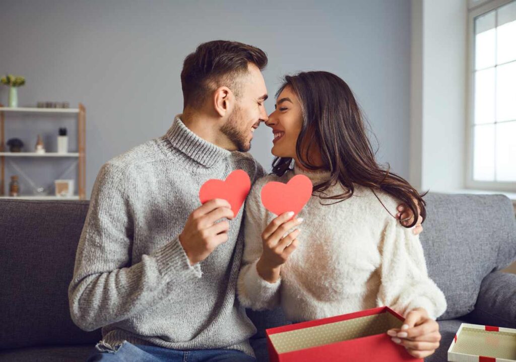 Man and  a woman celebrating valentines day. Both of them are holding paper hearts in their hands and look like they are in love.